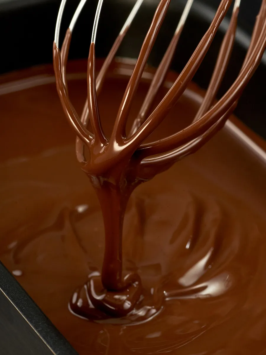 Melted chocolate dripping from a whisk, creating a rich, decadent texture.