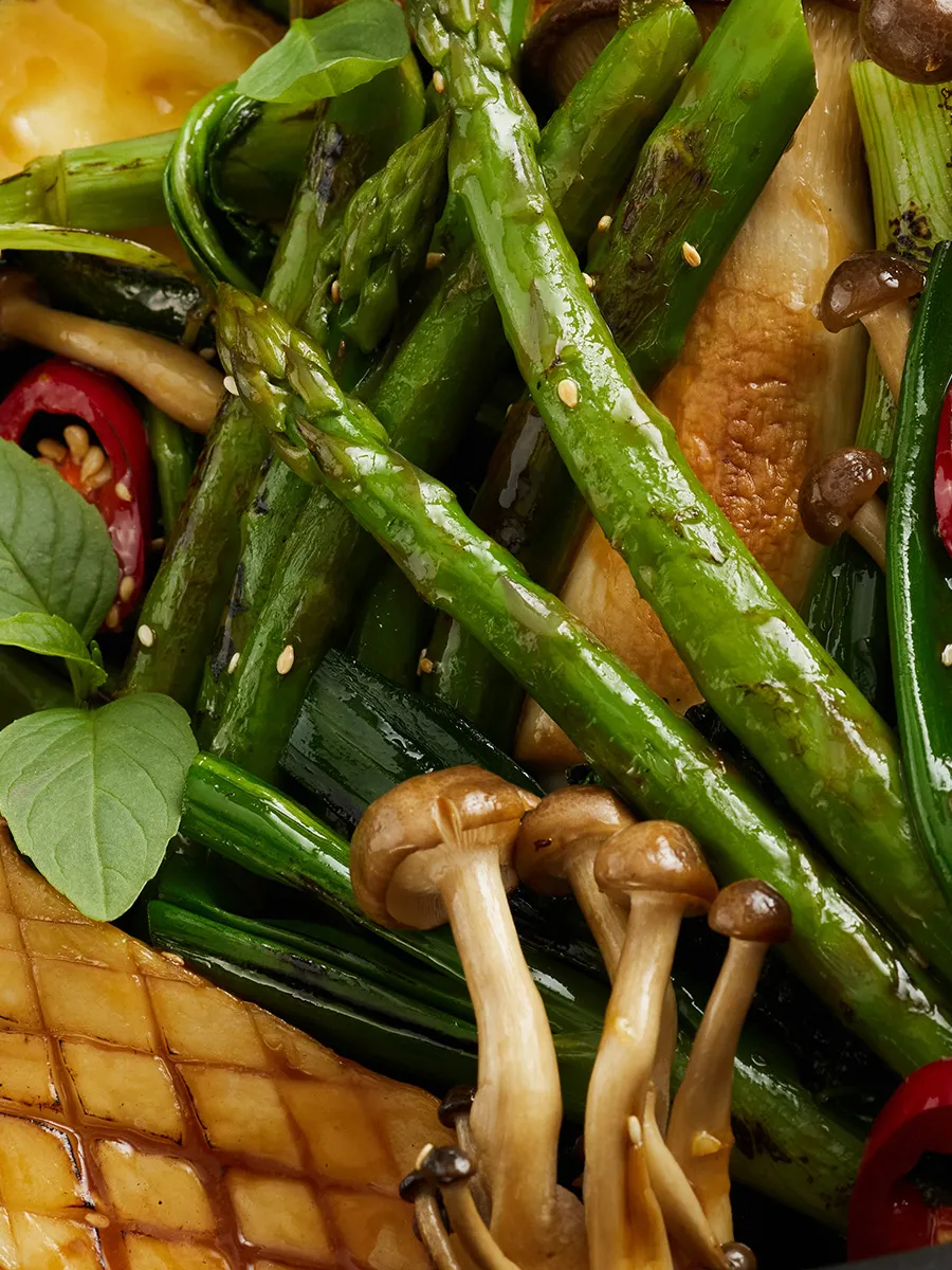 Grilled asparagus, mushrooms, and other vegetables on a wooden surface.