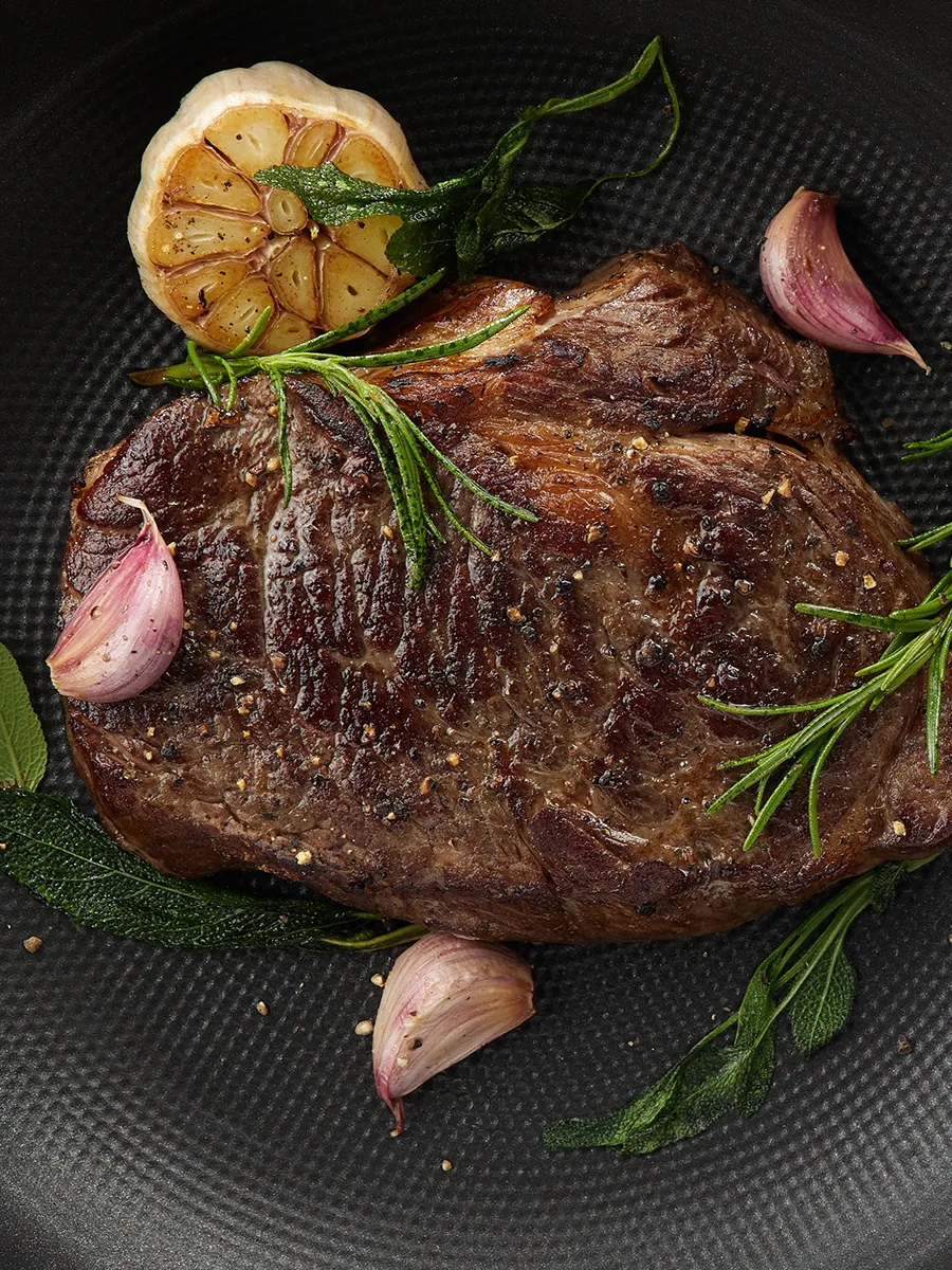 Grilled steak with rosemary, garlic, and lemon on a dark plate.