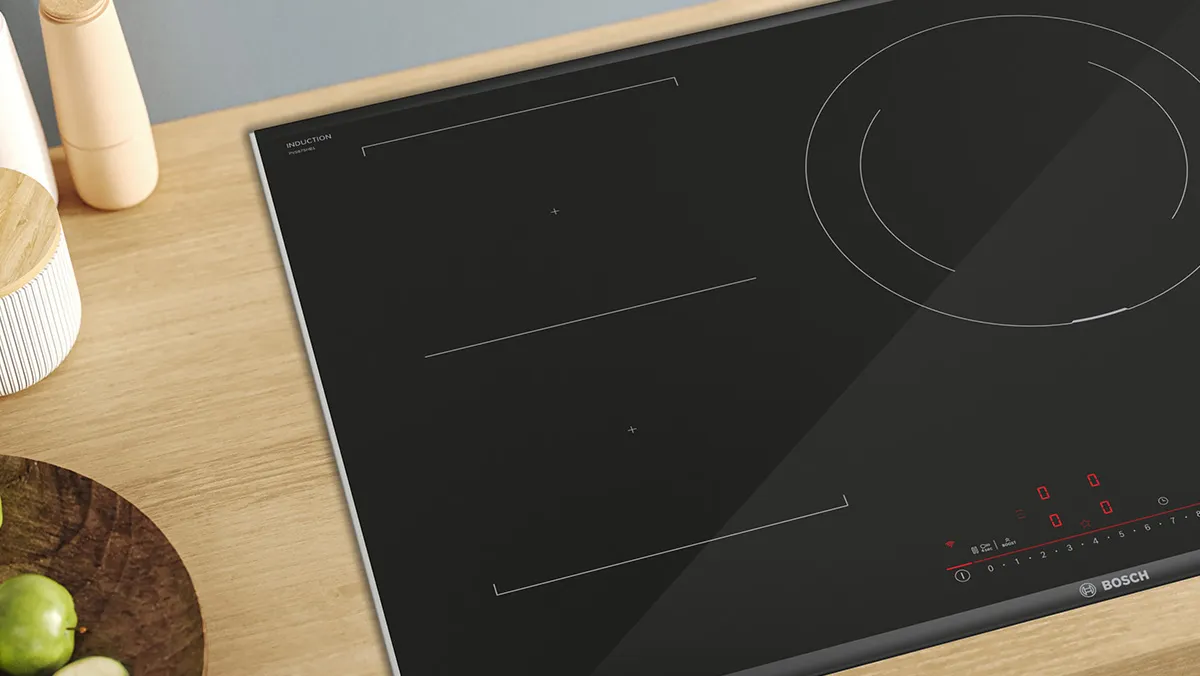 Induction cooktop with black glass surface, wooden cutting board, and green apple on kitchen counter.