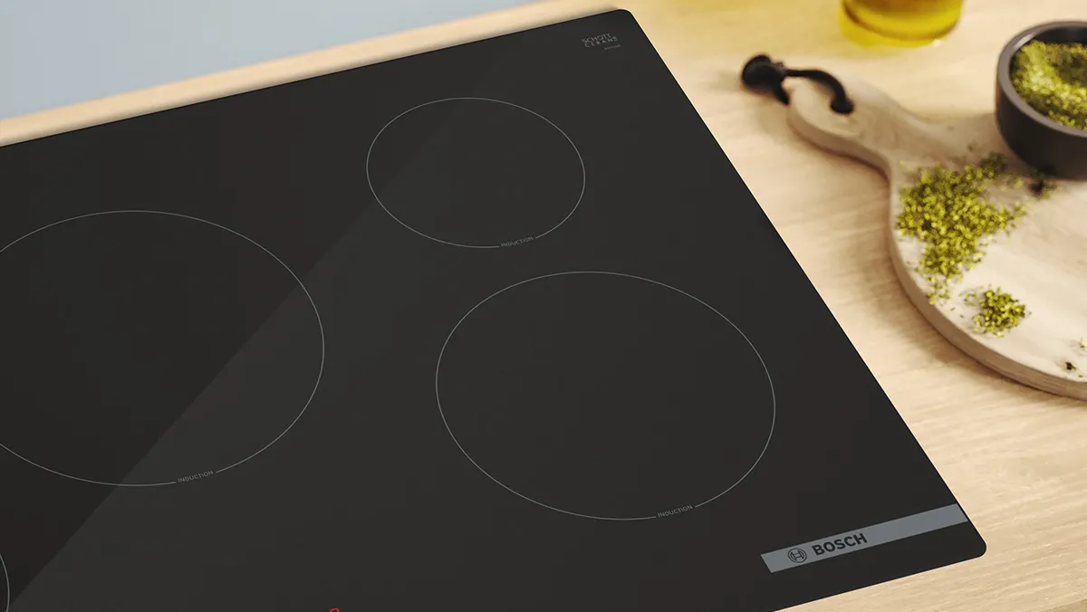 Black induction cooktop with four circular cooking zones on a wooden surface with cooking ingredients.
