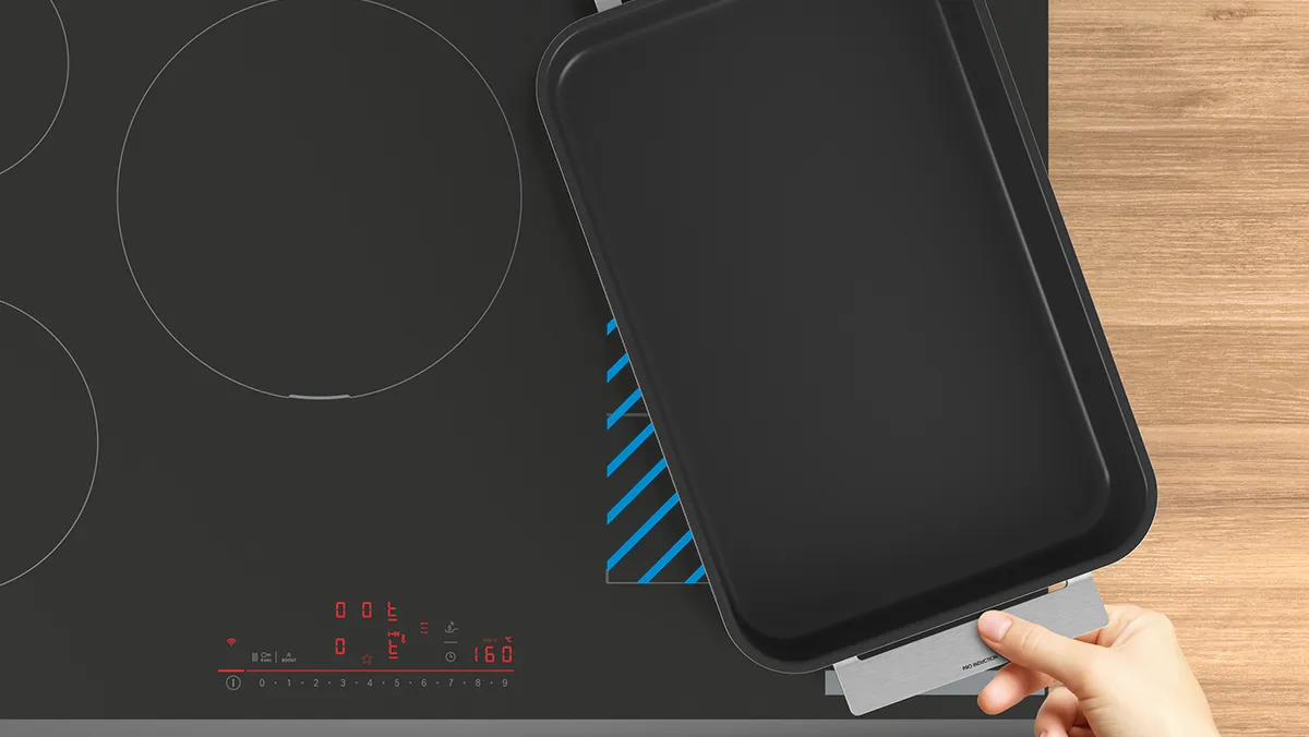 Black induction cooktop with smartphone on wooden surface.