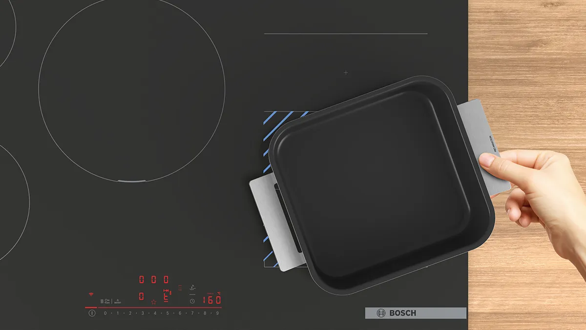 Black induction cooktop with hand placing black cooking pan on it.