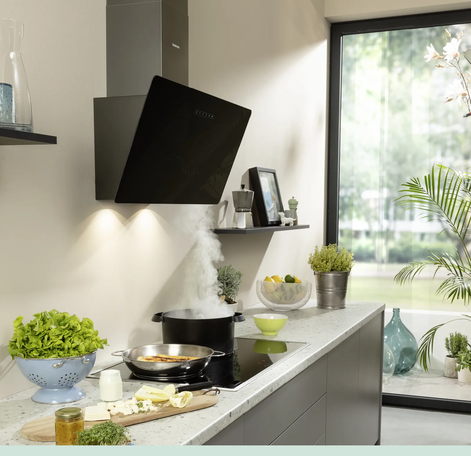 Eine schwarze Constructa Dunstabzugshaube saugt den Dampf von einem Topf und einer Pfanne auf dem Kochfeld ab.