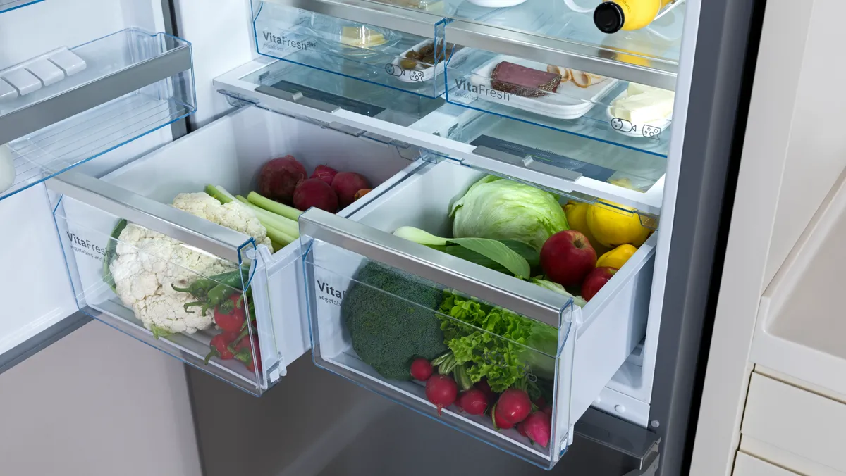 Open fridge freezer with drawer, stuffed with fresh ingredients.