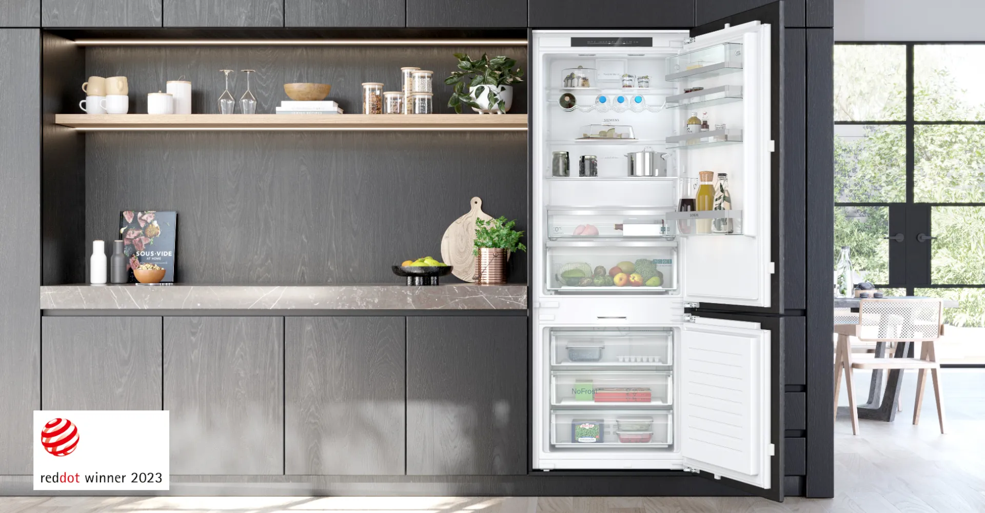Frigorifero combinato da incasso Siemens aperto con illuminazione brillante, perfettamente inserito in una cucina moderna e minimalista con mobili scuri e mensole in legno. In basso a sinistra è visibile il logo del premio Red Dot Winner 2023.