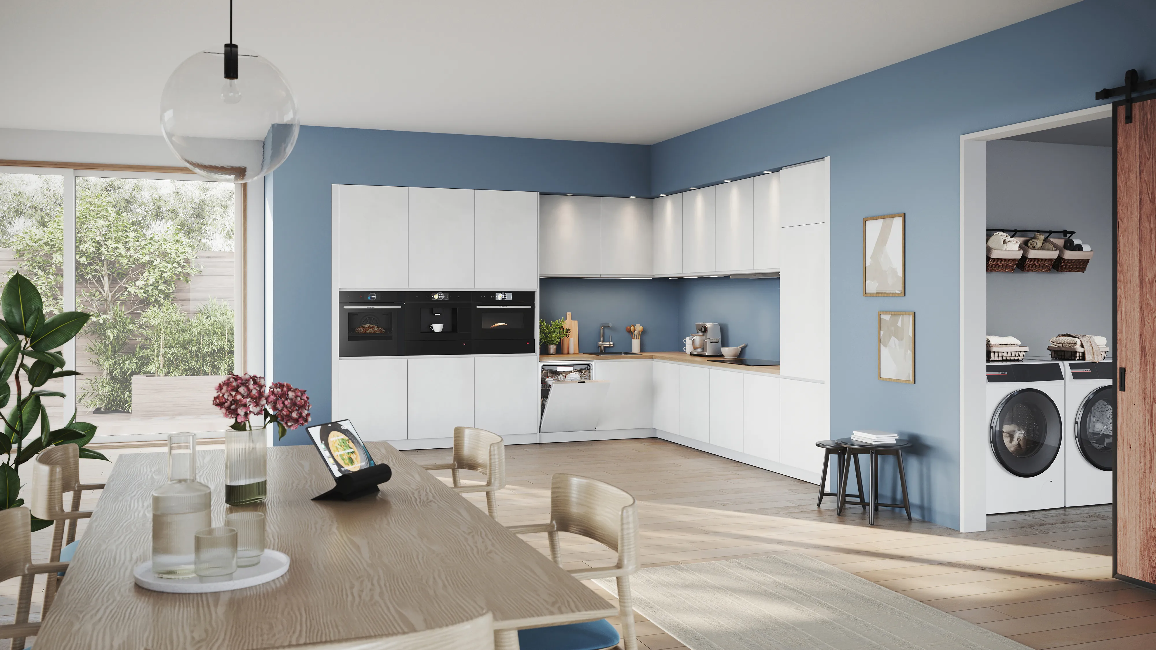 Cocina y comedor modernos de concepto abierto en tonos azules y blancos, con grandes ventanales, lámpara colgante, electrodomésticos, plantas y un rincón de lavandería.