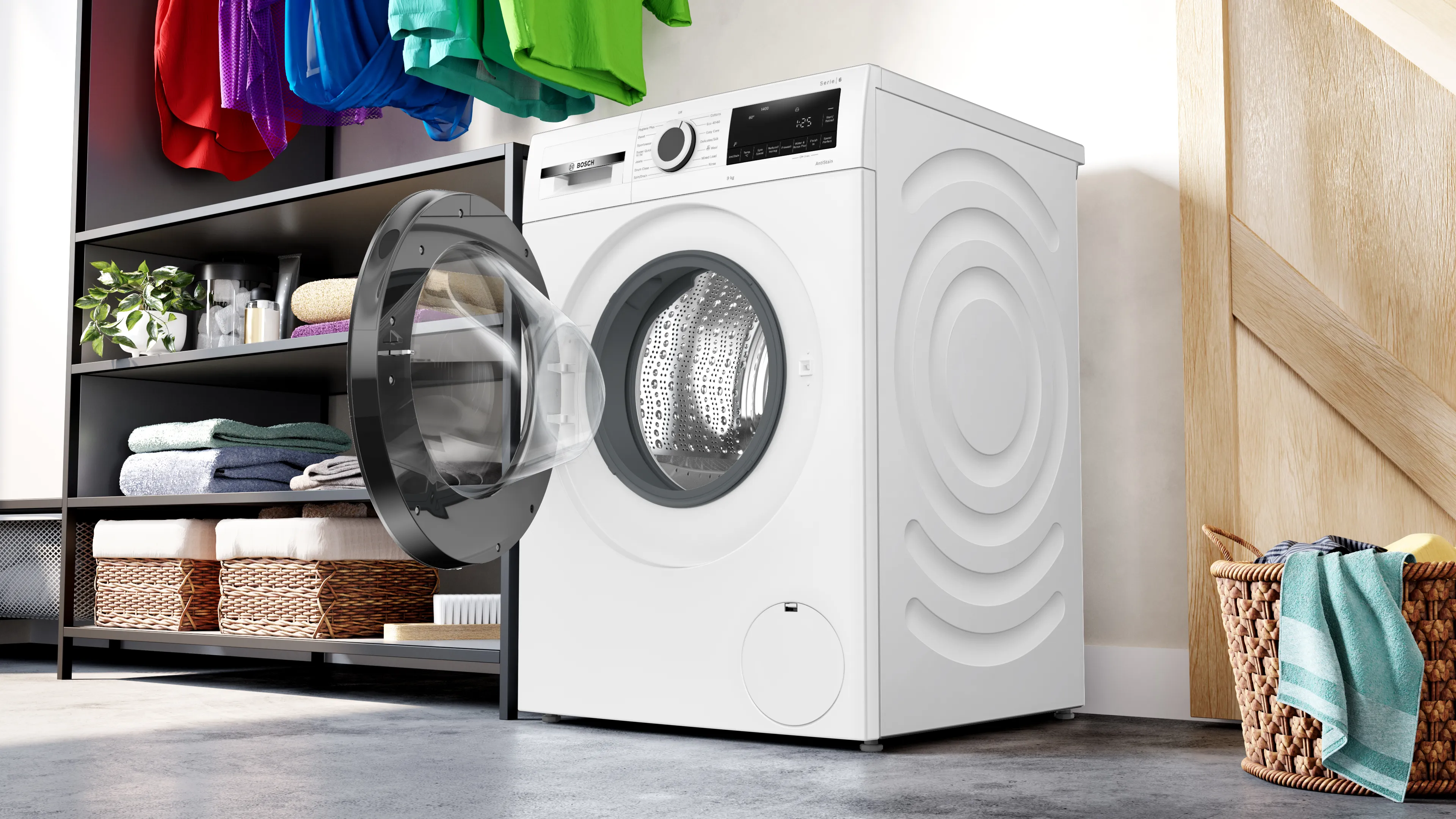 Washing machine in a laundry room with colorful clothes and storage shelves.