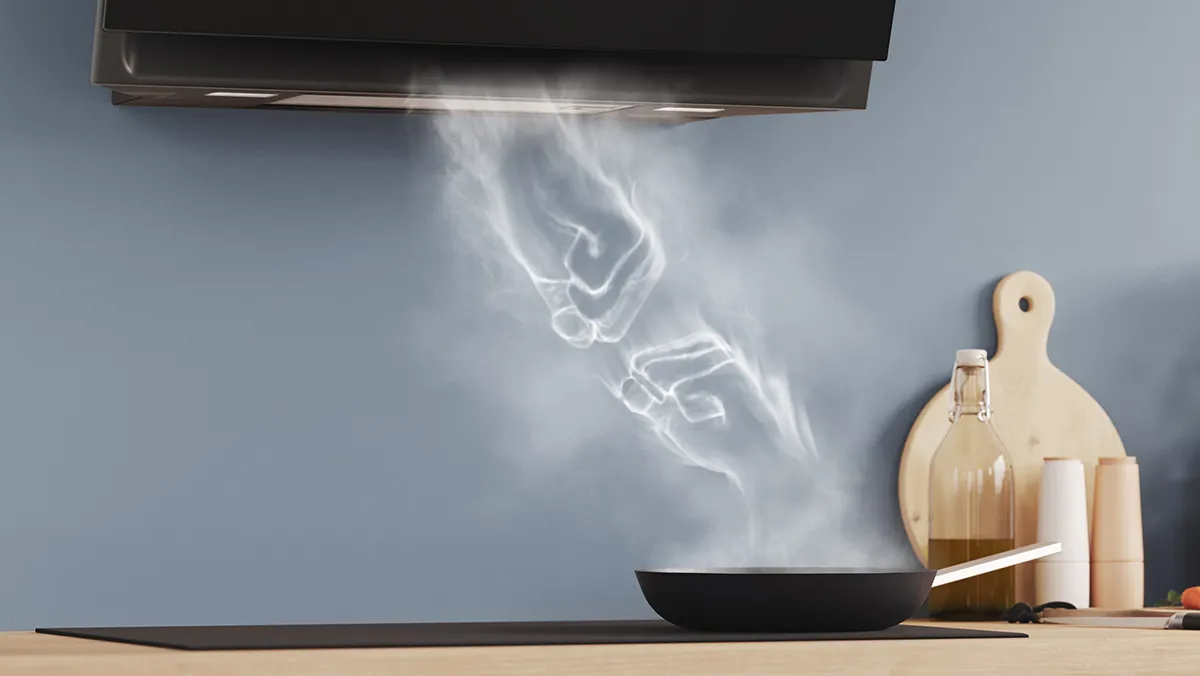 Smoke rising from a cooking pan on a wooden counter, with kitchen utensils and appliances visible.