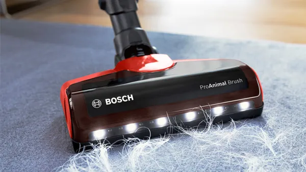 A close-up of a red and black Bosch "ProAnimal Brush" vacuum cleaner head with LED lights, actively cleaning white pet hair from a grey carpet.
