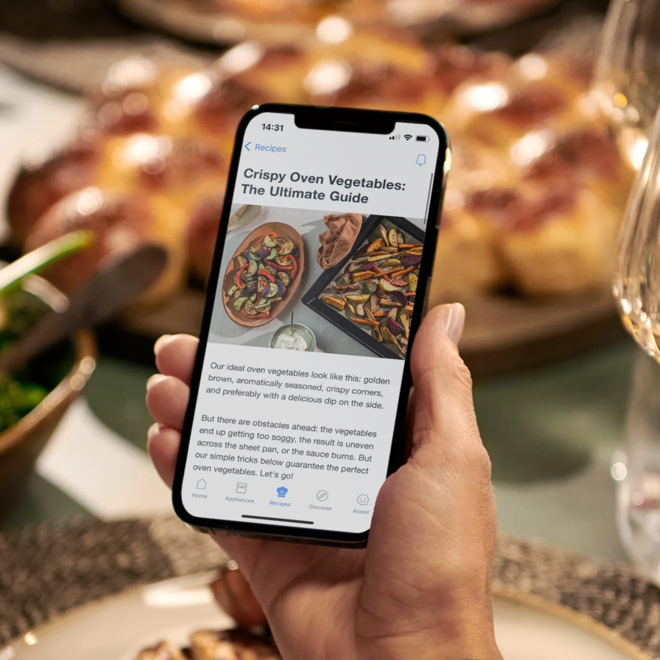 Smartphone displaying article on crispy oven vegetables, held in hand near pizza and other food items.