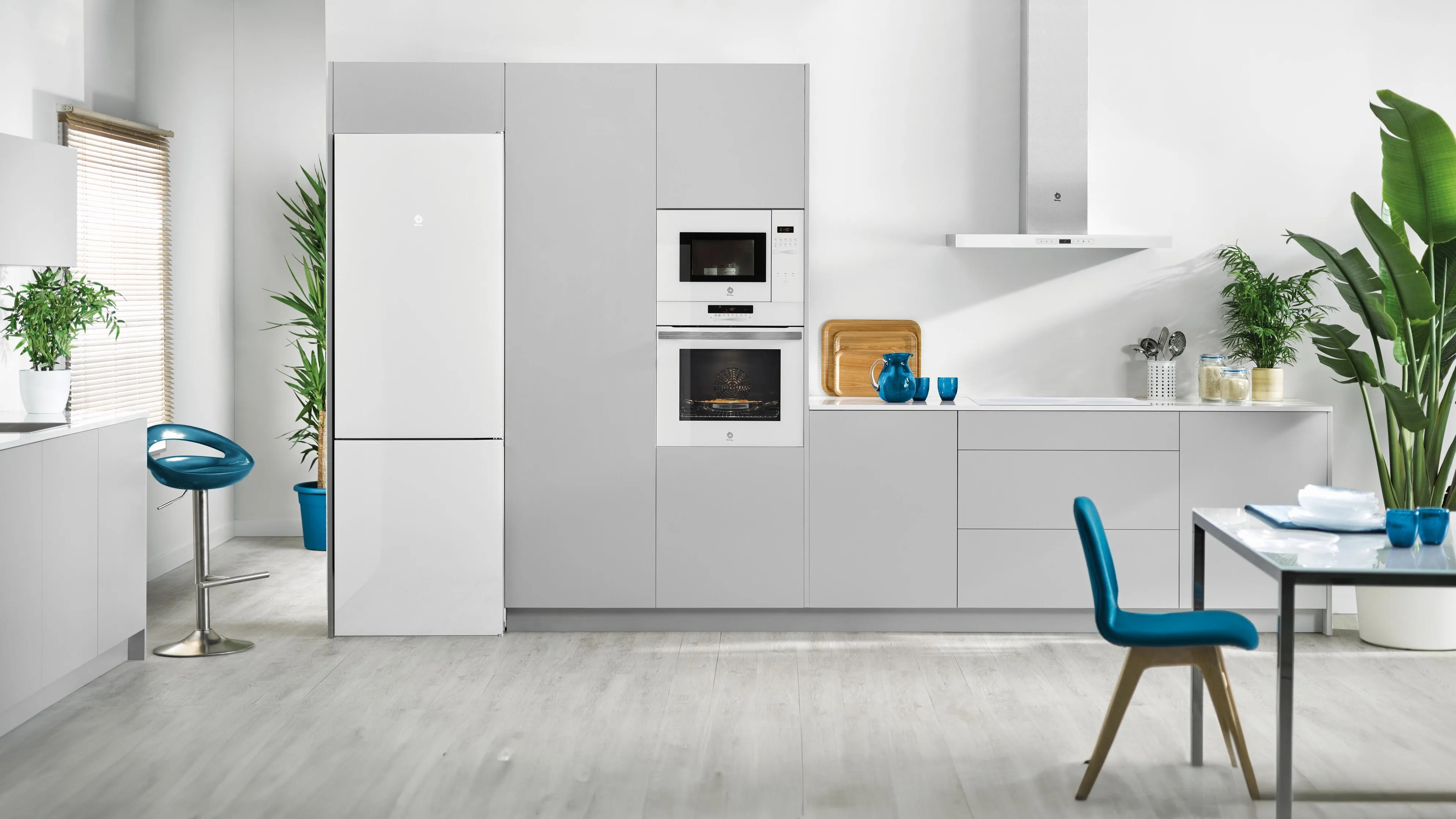 Cocina moderna y minimalista con muebles blancos, electrodomésticos de cristal blanco y detalles azules. 