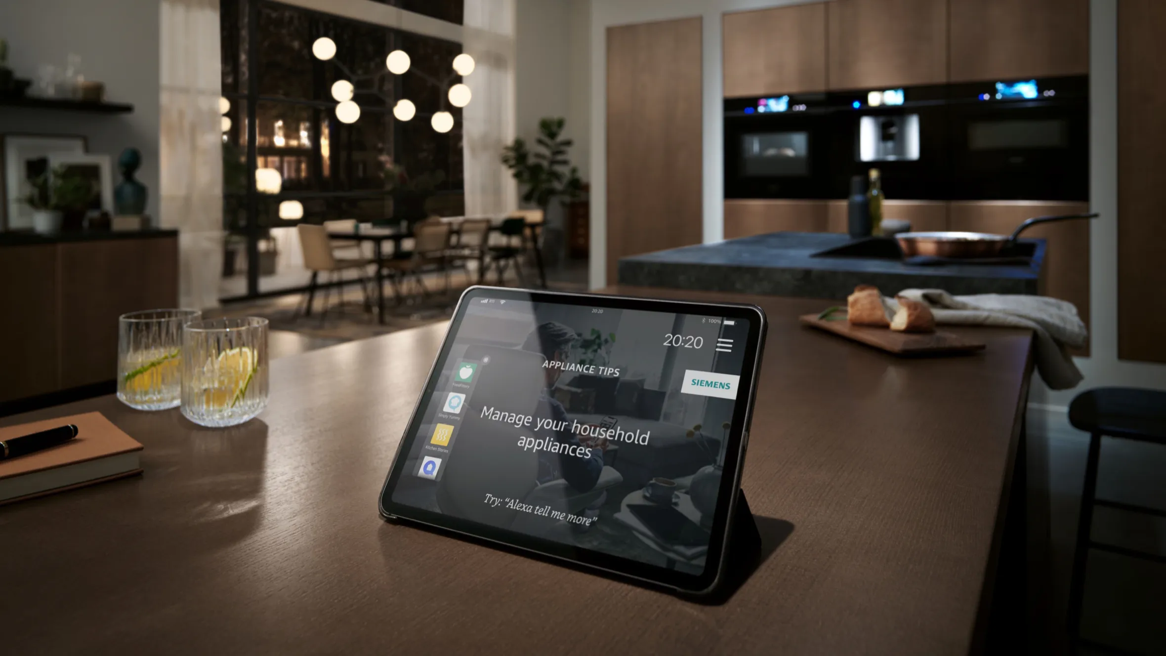 Une tablette de contrôle domotique posée sur l'îlot de cuisine affiche l'interface de gestion des appareils électroménagers, avec en arrière-plan une cuisine moderne et un coin repas.