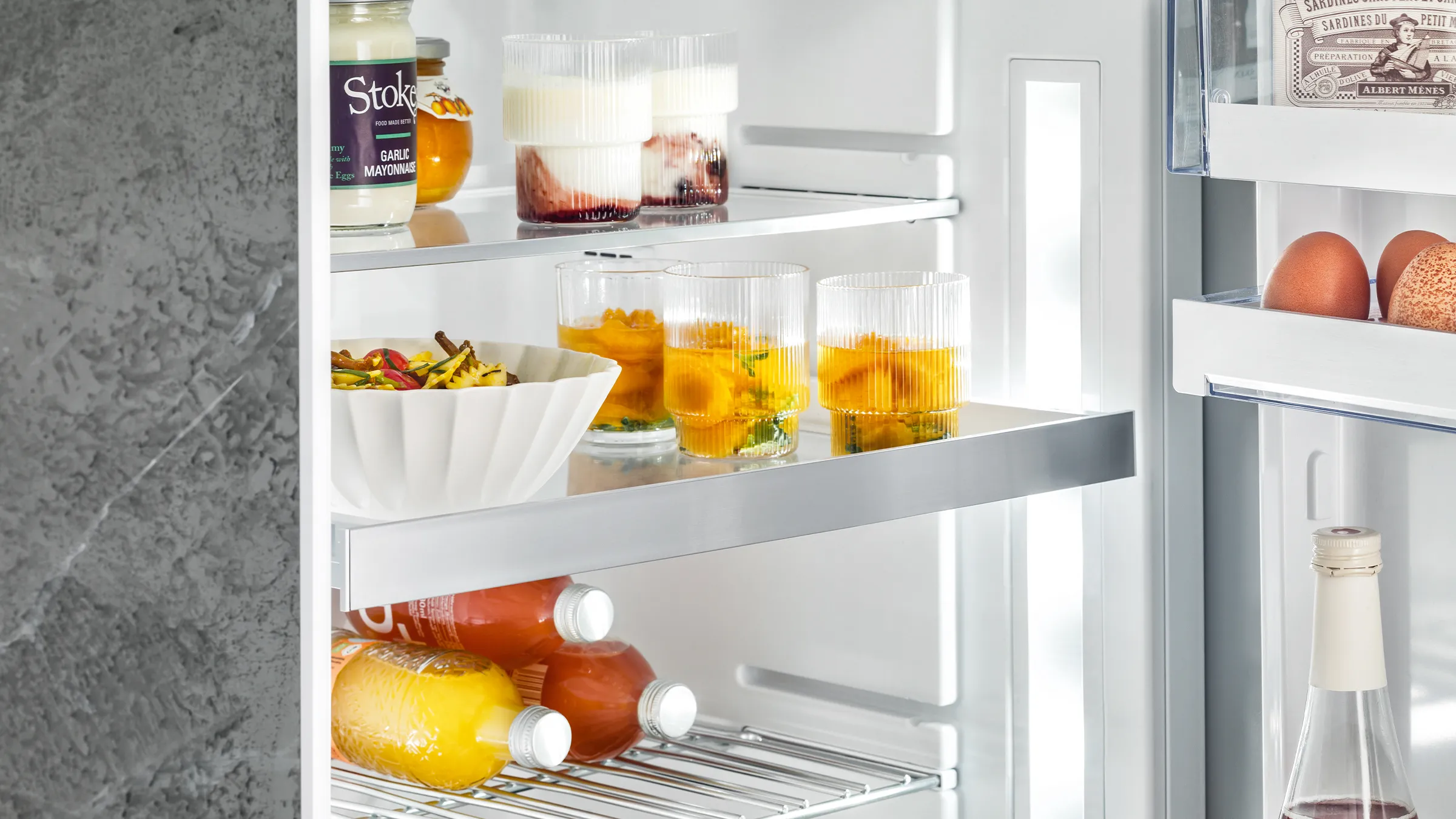 Open refrigerator with various food items, including fruits, vegetables, and condiments, neatly organized on the shelves.
