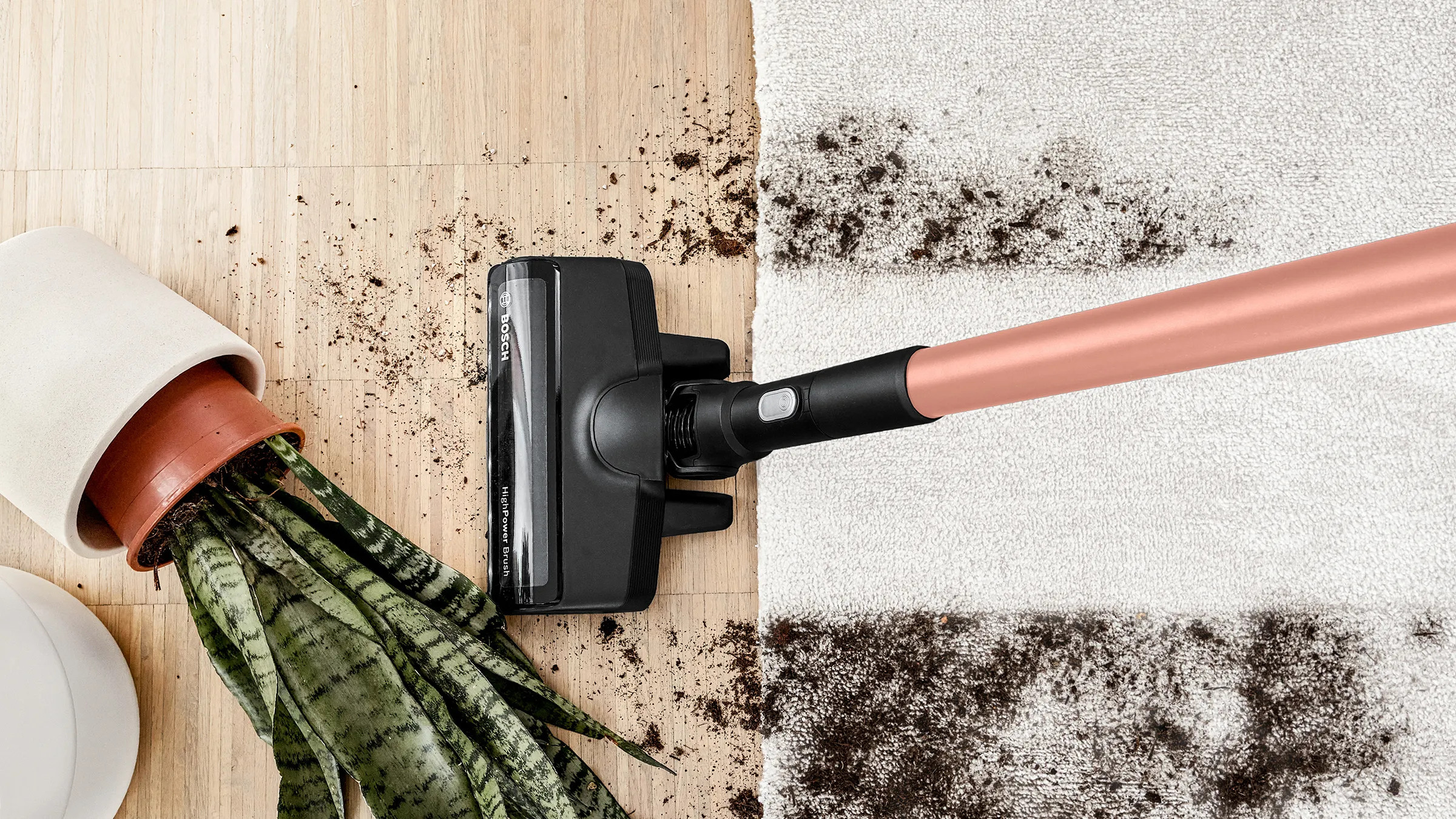 A vacuum cleans soil spilled from a knocked over pot plant on a carpet and hard floor.