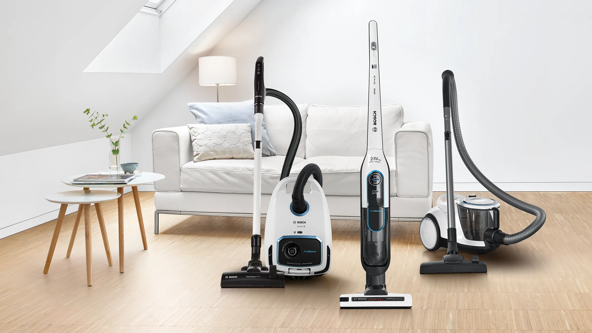 A range of ProSilence vacuums stand in a bright white attic space with a couch and side table.