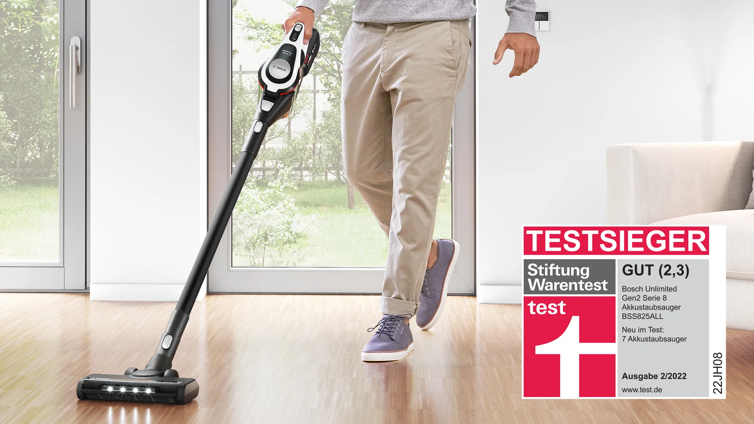 The Stiftung Warentest badge, indicating a test winner, is superimposed on a shot of a man using a stick vacuum to clean hard floors.