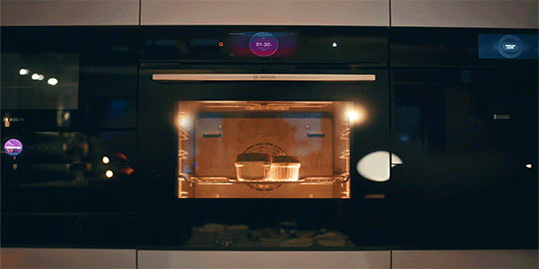 A view across a dining room table into a bright, modern kitchen full of Bosch appliances.
