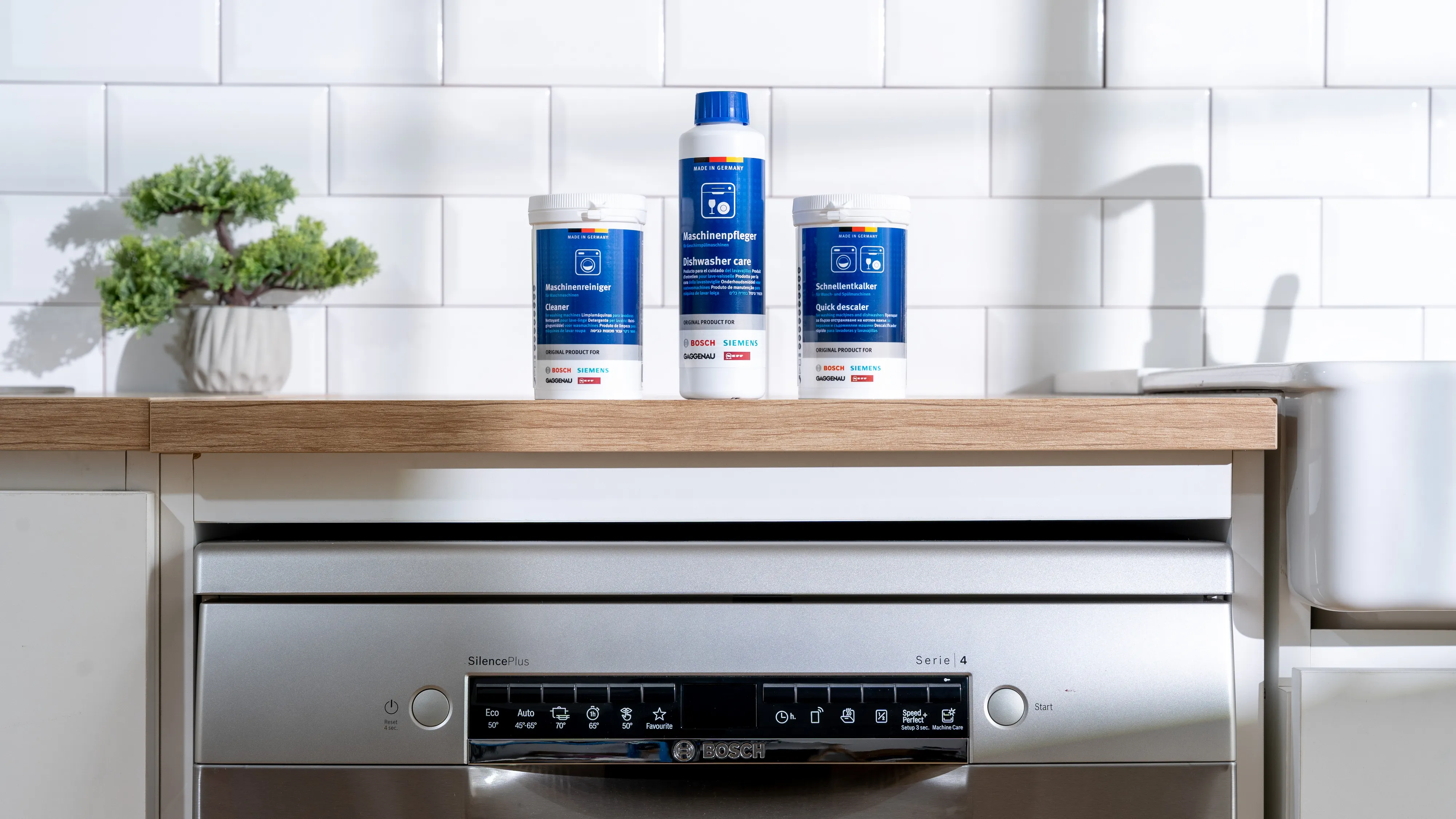 Bosch dishwasher with cleaning products, potted plant, and wooden shelf in a modern kitchen setting.