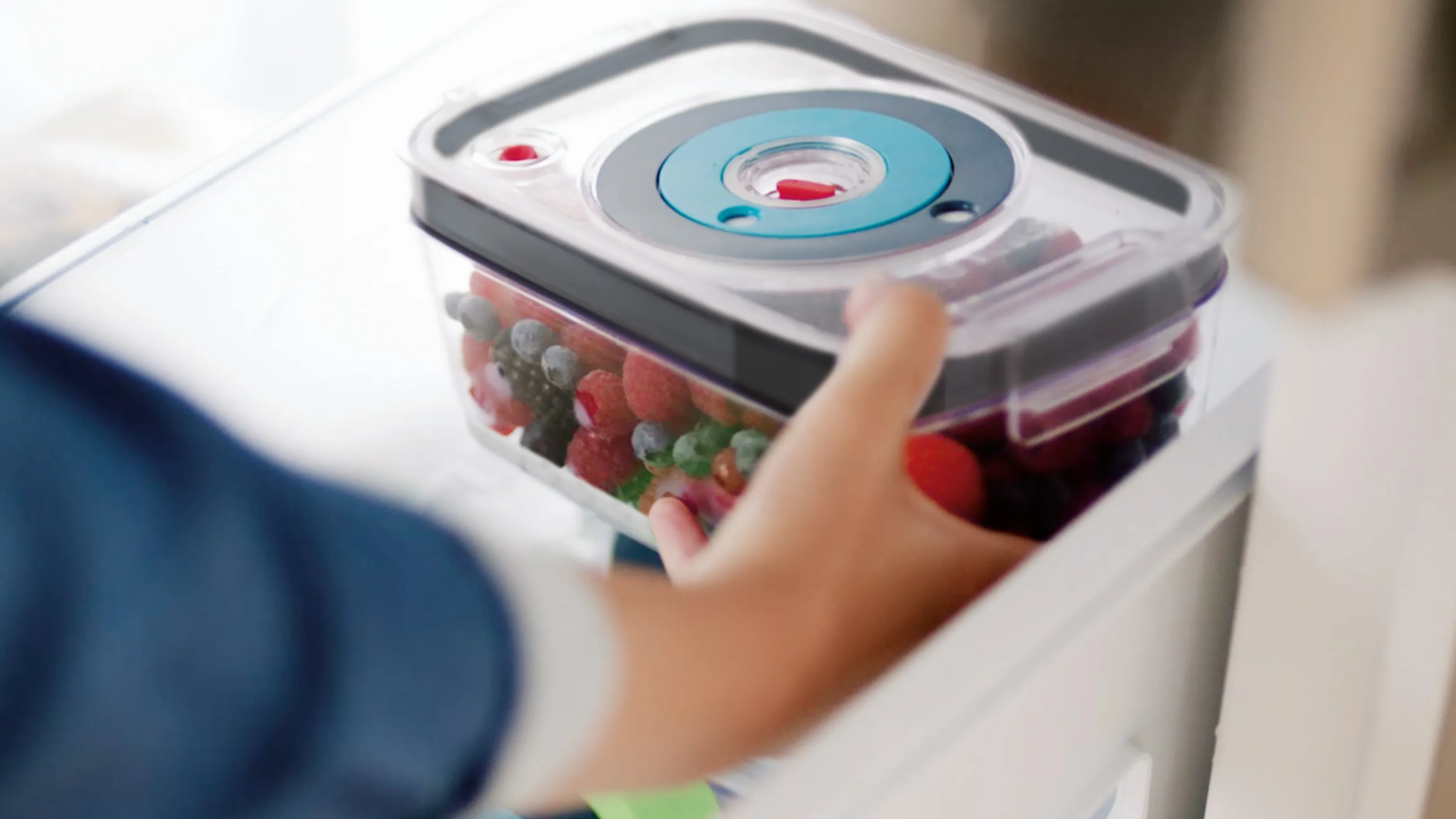 Vakuum-Food-Behälter mit frischen Produkten innen, von einer Hand geöffnet.