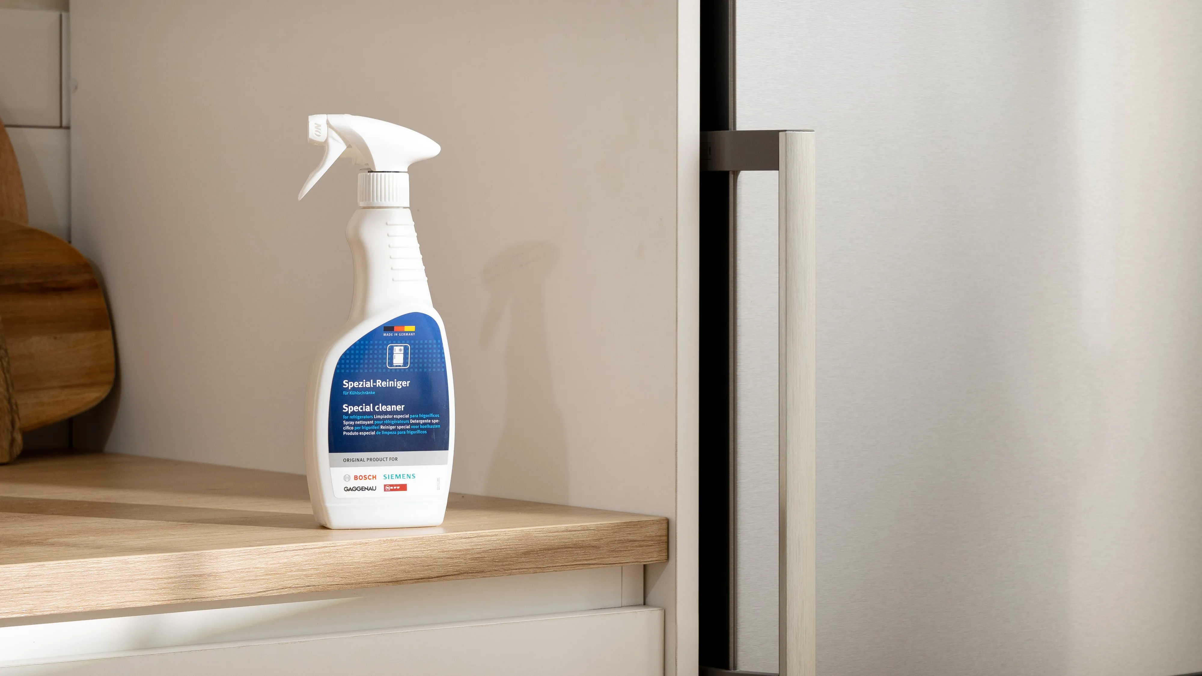 Sprühflasche von Oberflächenreiniger auf Holzregal, Kühlschrank im Hintergrund.