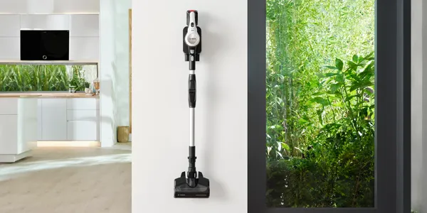 Beyaz duvarda monte edilen Cordless vakum, cam yoluyla görünür yeşil foliage ile.