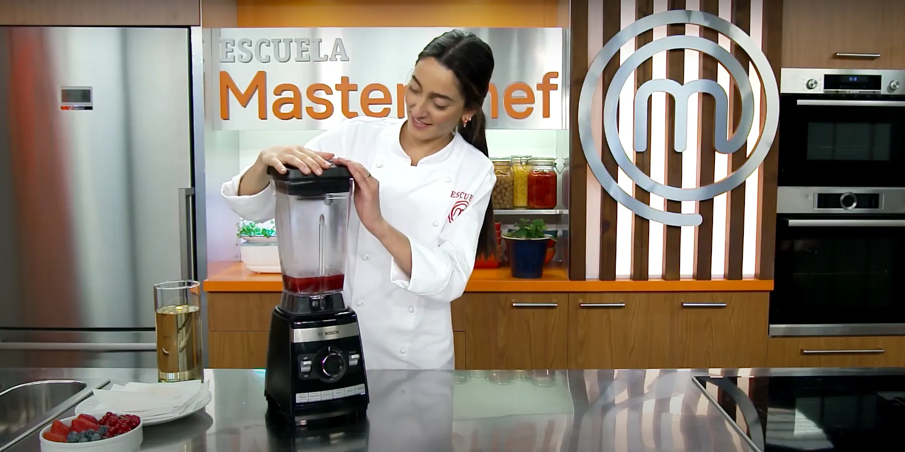 Mujer con uniforme de chef usando licuadora en cocina con la marca Escuela Masterchef.