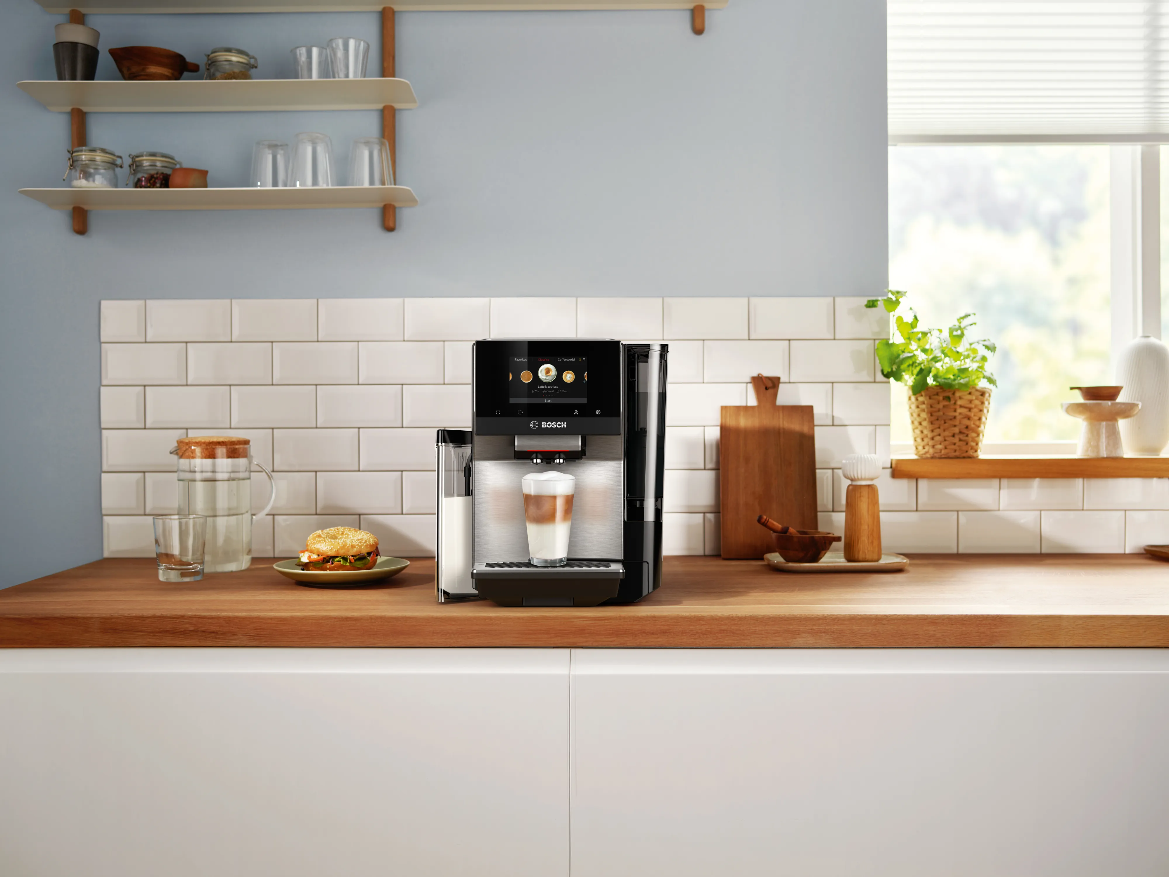 Bosch coffee machine on a wooden countertop in a bright kitchen with a latte and food nearby.