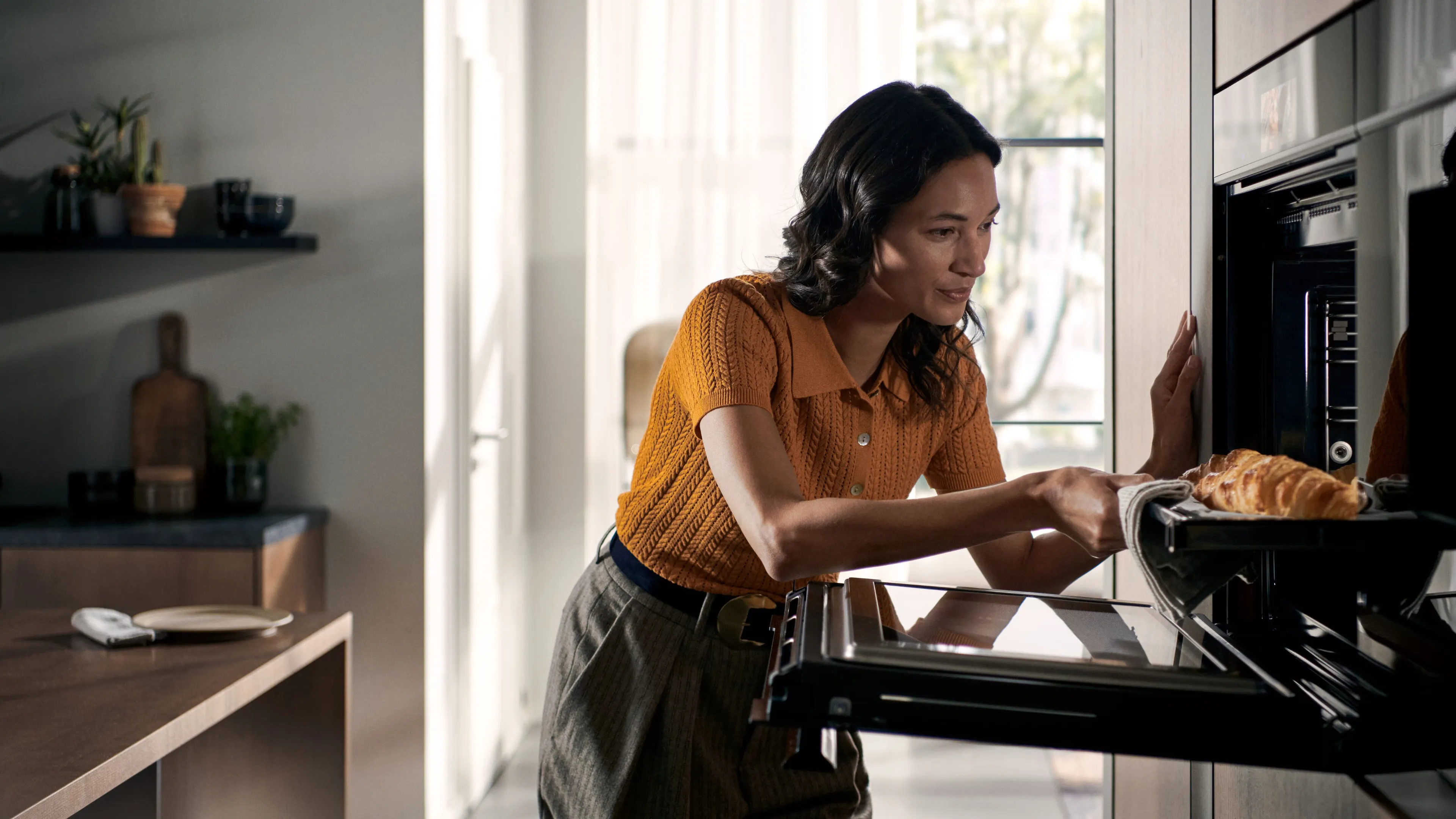 Femme plaçant un plateau de nourriture dans un four encastrable Siemens dans une cuisine moderne.