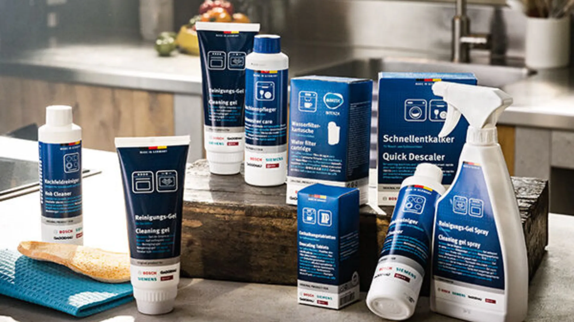 Diverse reinigings- en onderhoudsproducten en roze bloemen op een wit werkblad in een houten keuken.