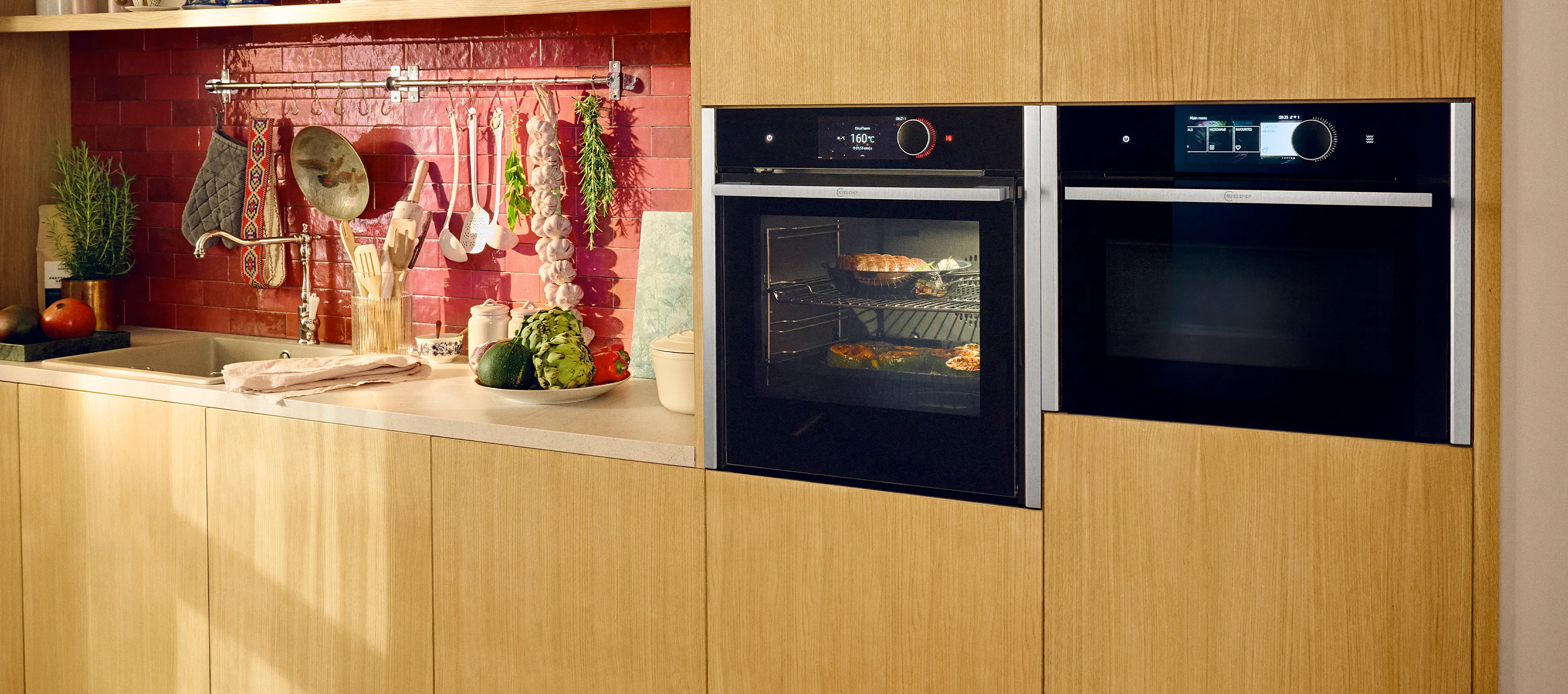 Zwei Backöfen in Metallic Silver nebeneinander in einer Küche mit Holz und roten Fliesen. 