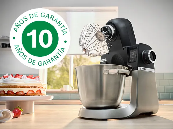 Imagen muestra la batidora de pie Serie 6 sobre la encimera de la cocina, junto a numerosas bolas de masa y el logotipo de garantía de 10 años superpuesto.