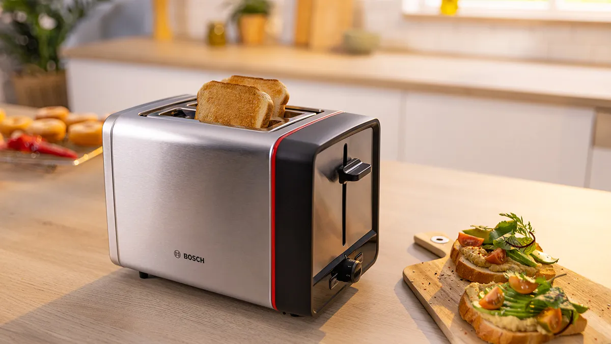 Máy nướng bánh mì bằng thép không gỉ với những lát bánh mì nướng bên cạnh một lát bánh mì nướng phủ cá hồi và bơ trên quầy bếp. 