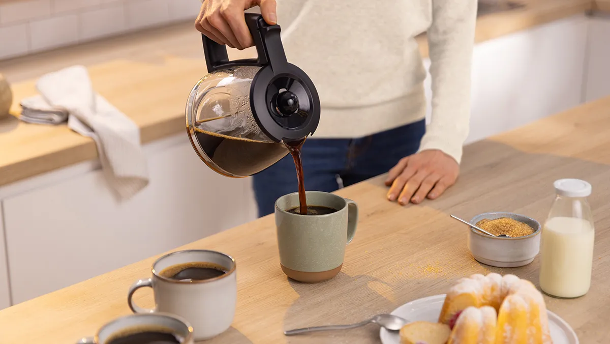 Person pouring coffee into a mug on a table with pastries and other breakfast items.