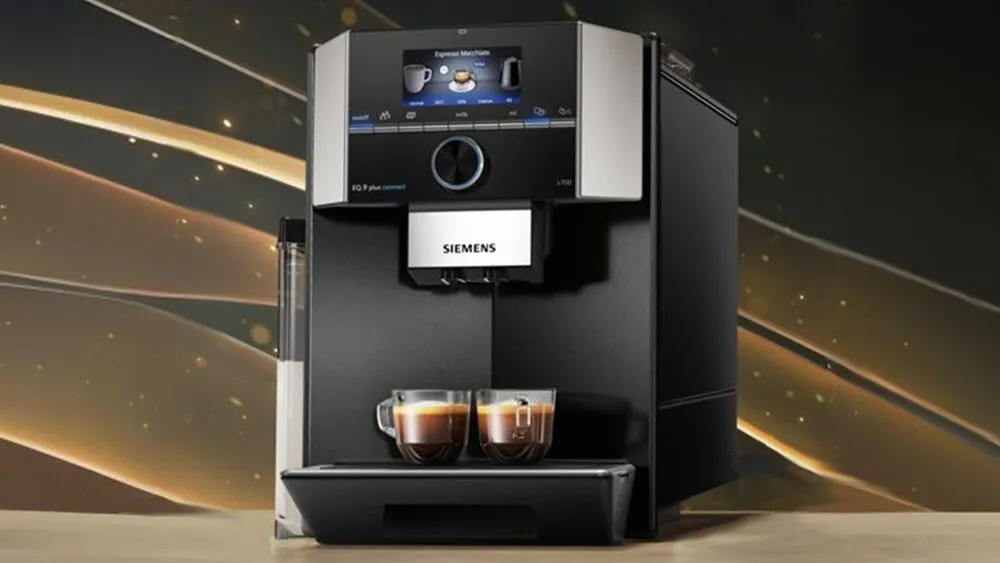 Sleek black coffee machine with digital display and two coffee cups on a golden background.