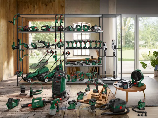 Garage gevuld met diverse groene elektrisch gereedschap, grasmaaiers, en tuinuitrusting op planken.
