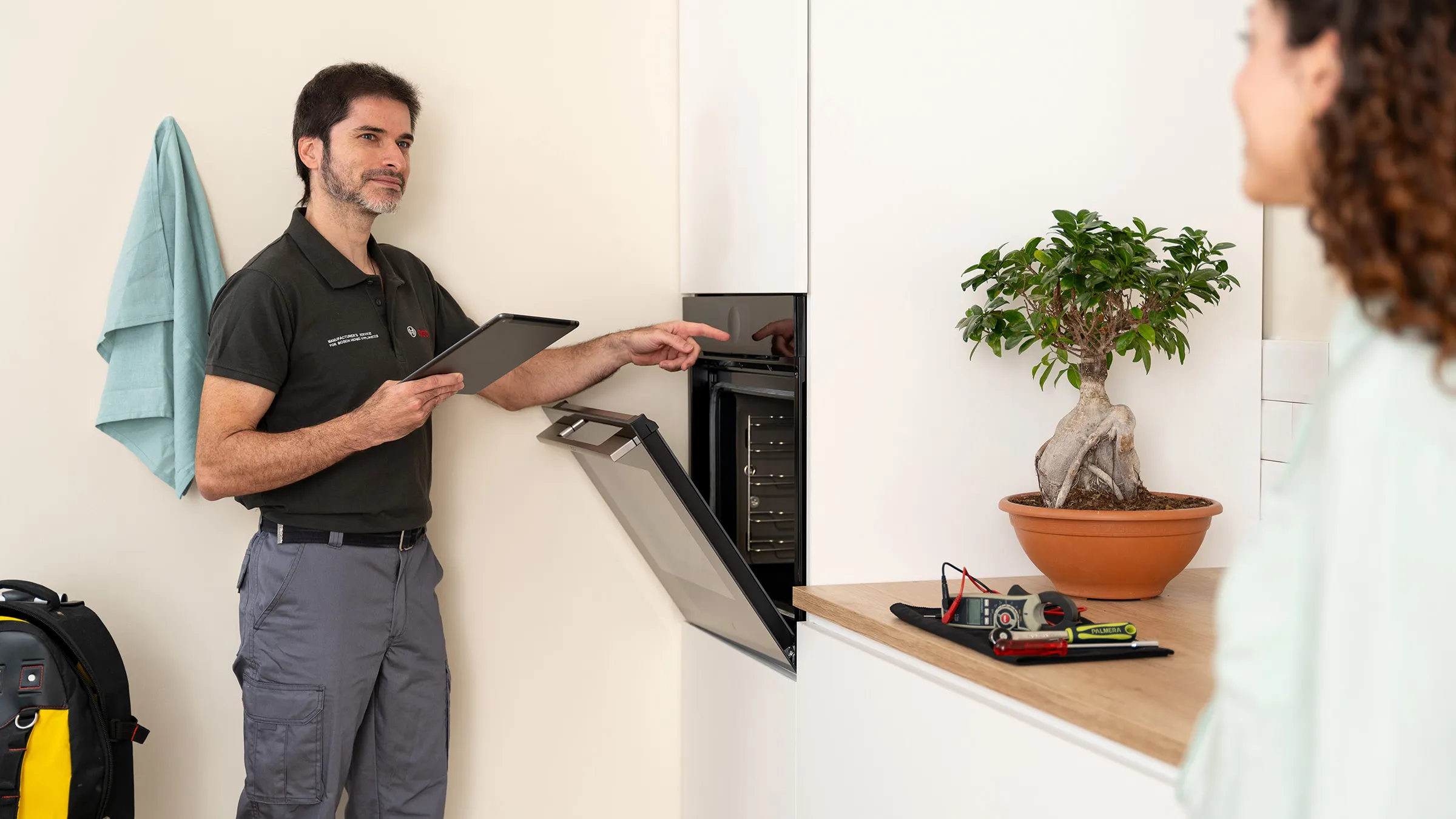 Technician inspecting a microwave oven while a woman observes nearby in a modern kitchen setting.