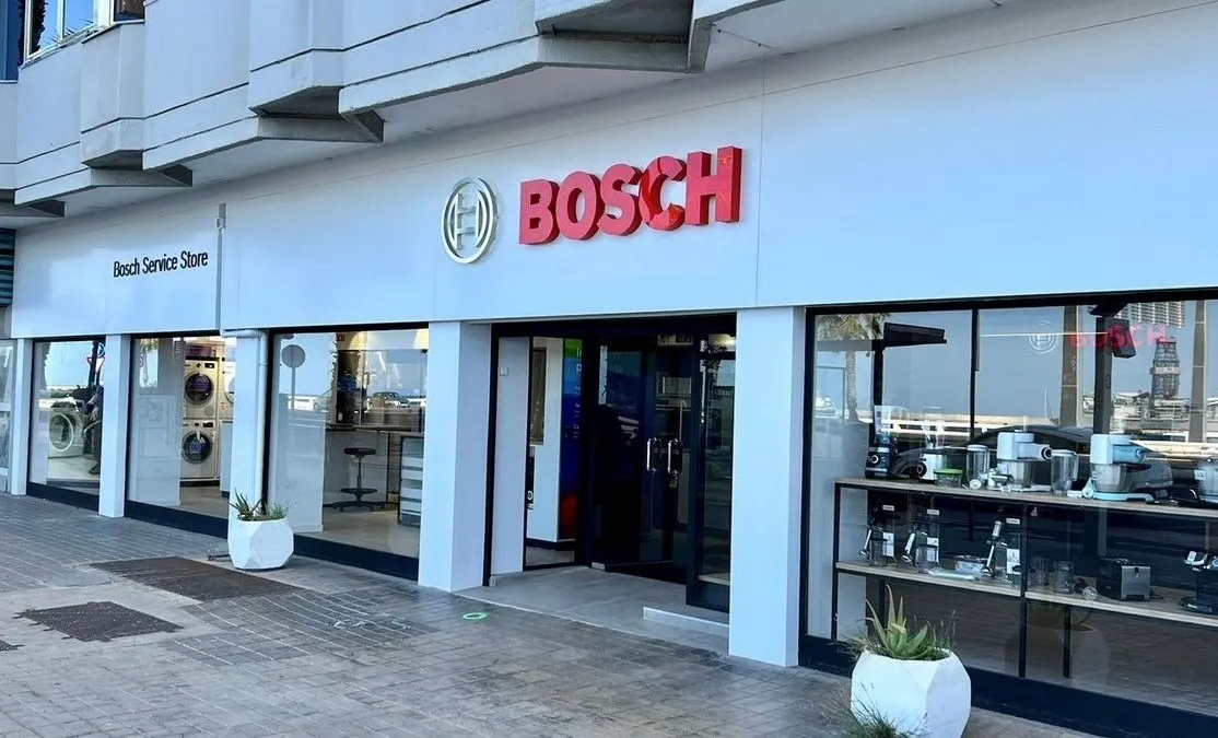 Un local de Bosch Service Store impecable, con el logotipo rojo de Bosch, amplios escaparates de cristal y una entrada central abierta, situado en una soleada calle urbana.