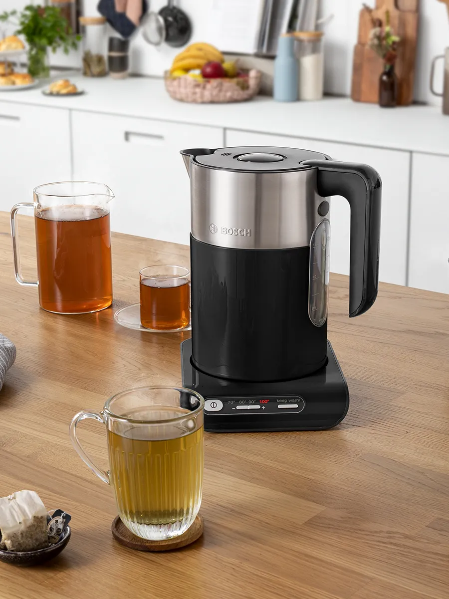 ხის დახლზე მდგარი შავი და უჟანგავი ფოლადის Bosch-ის ელექტრო ქვაბი, იქვე ჩაის ჭიქებით.