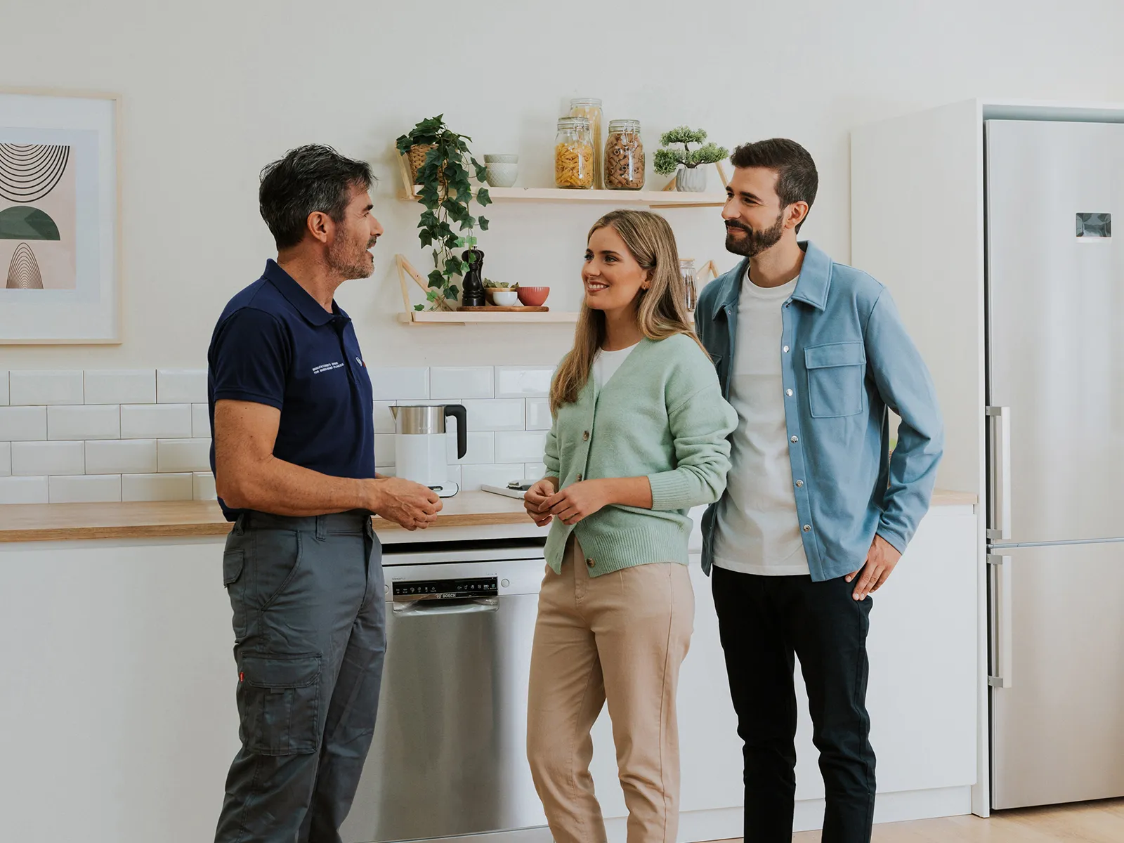A young couple consults with a technician in a bright, modern kitchen full of Bosch appliances.