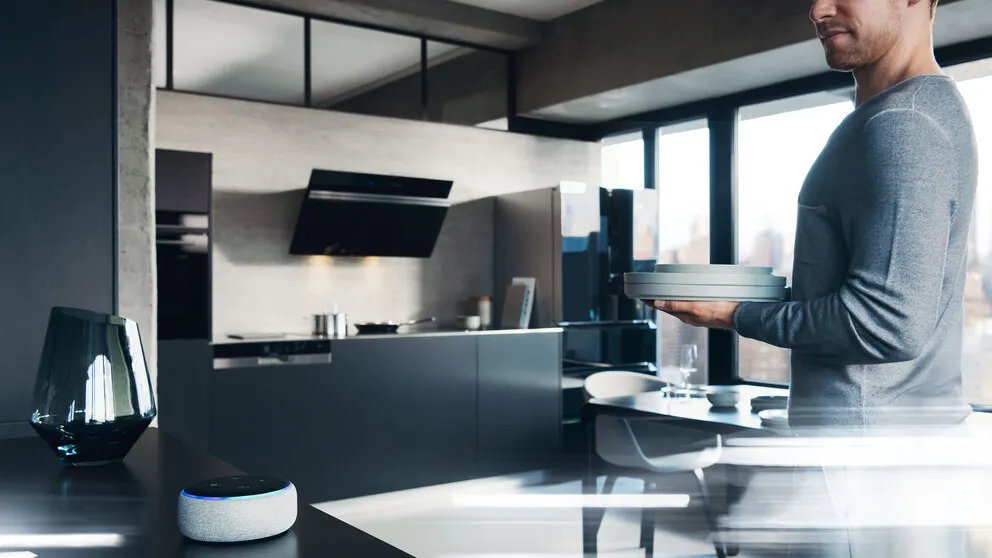 Man moving plates in the kitchen, standing by an amazon echo