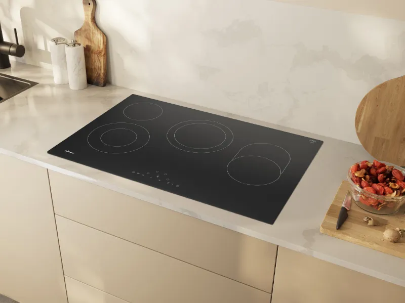 Modern kitchen with black electric cooktop, wooden cutting board, and glass bowl of ingredients.
