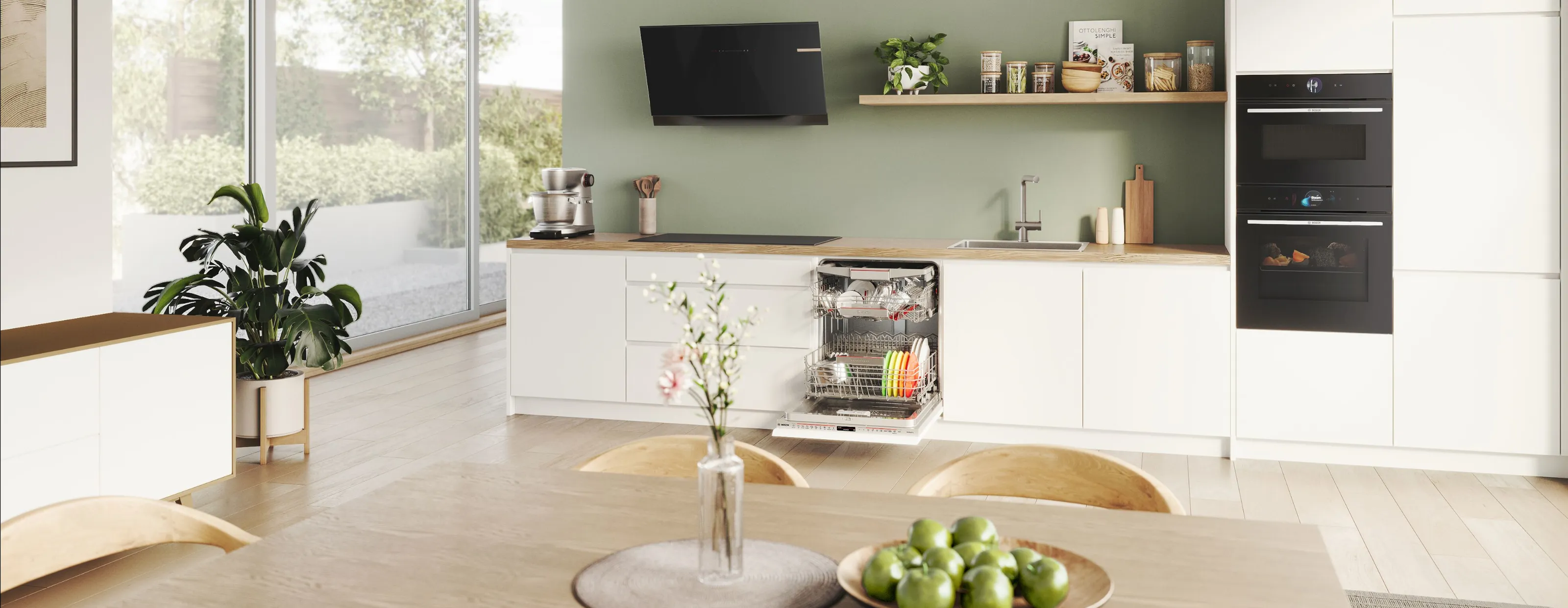 Cucina moderna con armadi bianchi, accenti di legno, elettrodomestici e grandi finestre con vista sul verde.