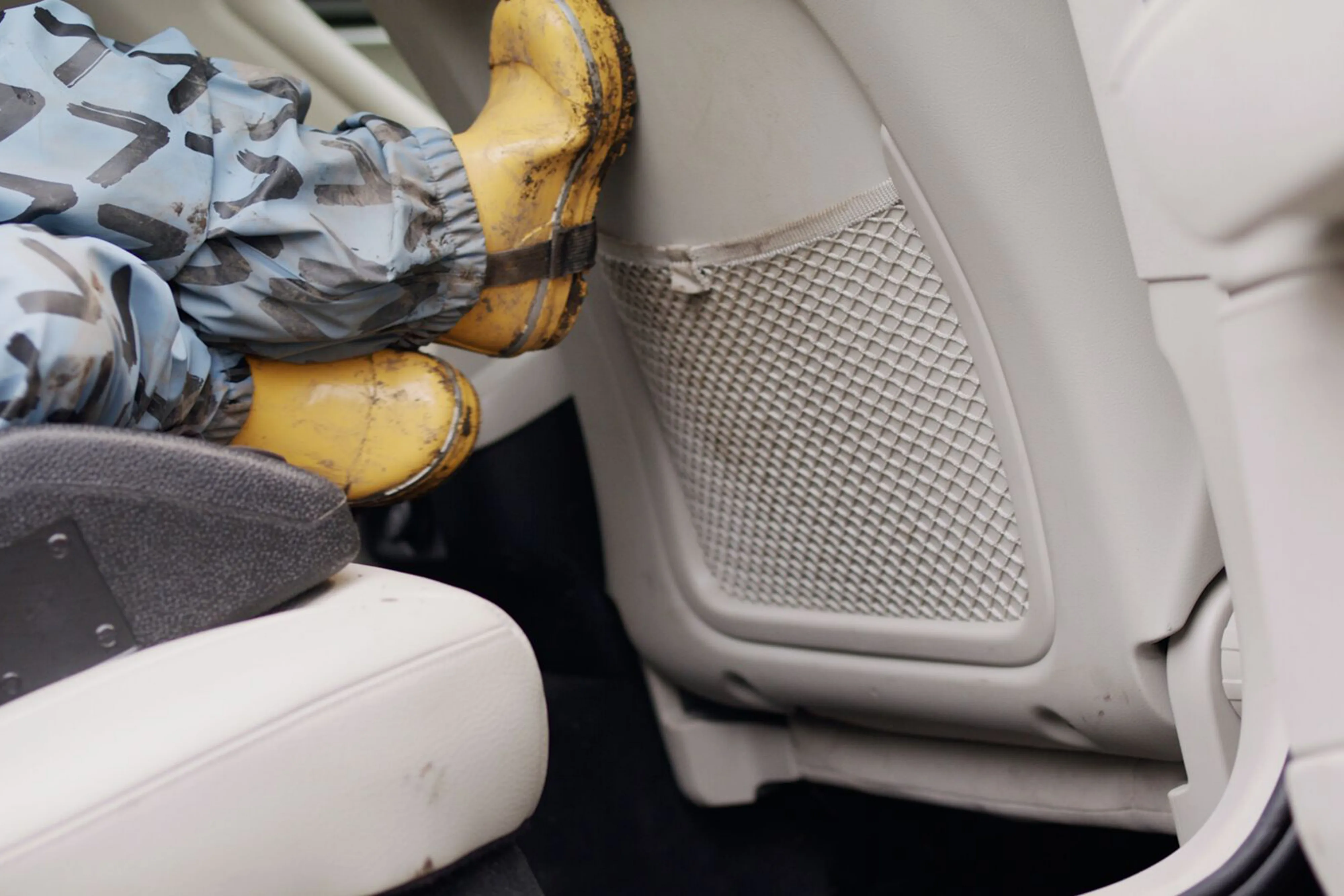 Child putting muddy shoes on back of car seat