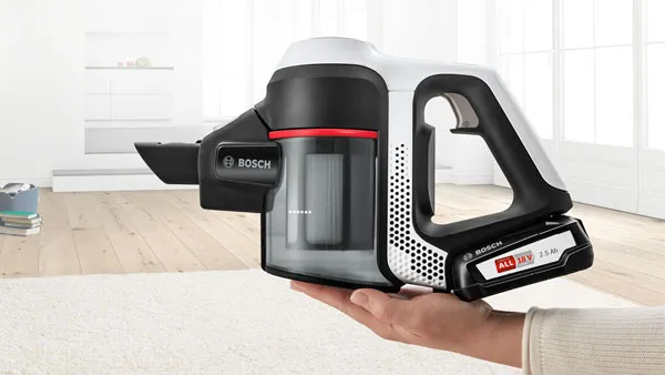 A hand holds the white and black Bosch cordless vacuum cleaner's handheld unit, showcasing its compact design and removable battery.