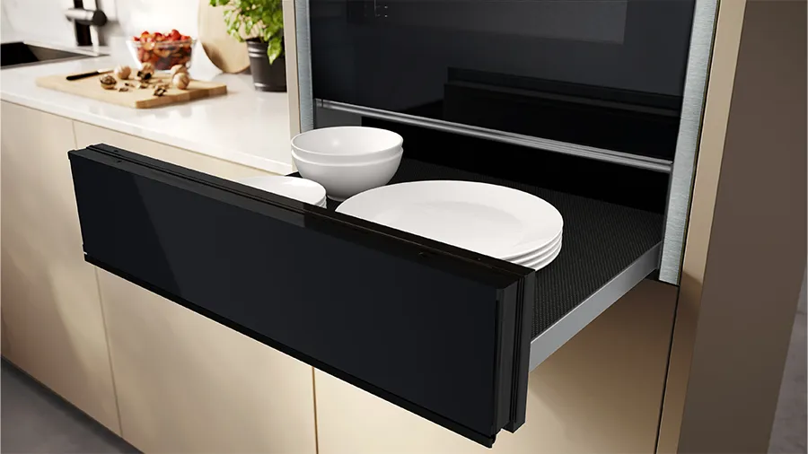 Un tiroir de cuisine moderne et élégant s'ouvre pour révéler des assiettes et des bols blancs, mettant en avant une solution de rangement organisée et stylée.