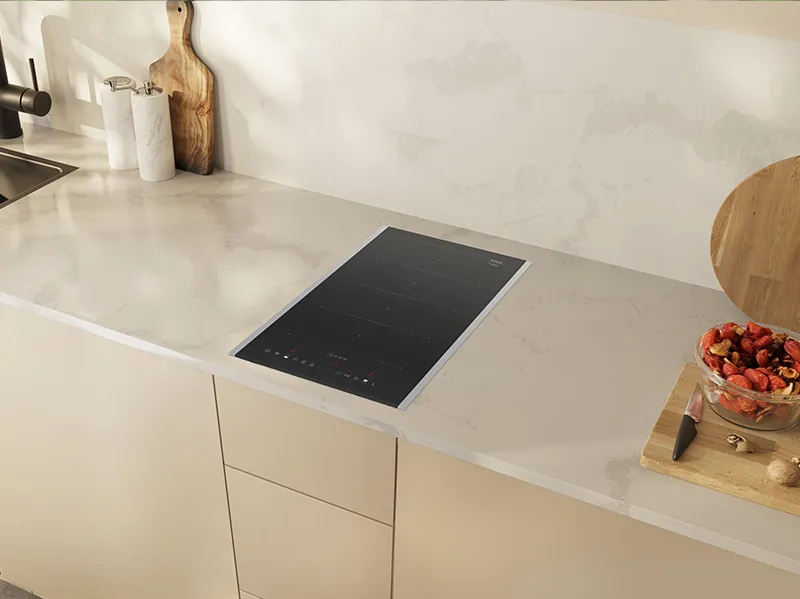 Modern kitchen countertop with induction cooktop, wooden cutting board, and bowl of fresh produce.