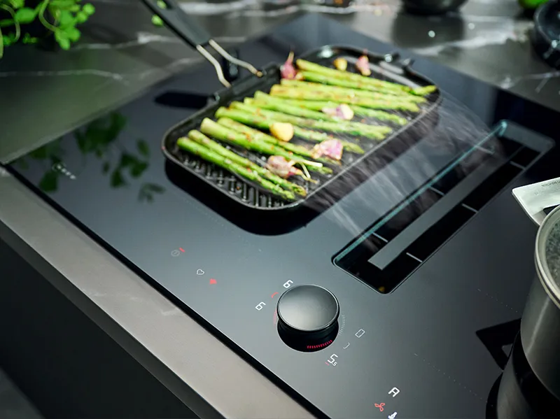 Grill pan of asparagus and bacon on a black induction cooktop near a control knob.