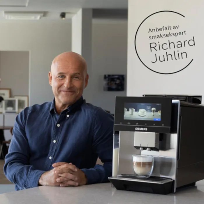 En mann i blå skjorte sitter ved en Siemens kaffemaskin med en nybrygget latte, i et moderne kjøkken.