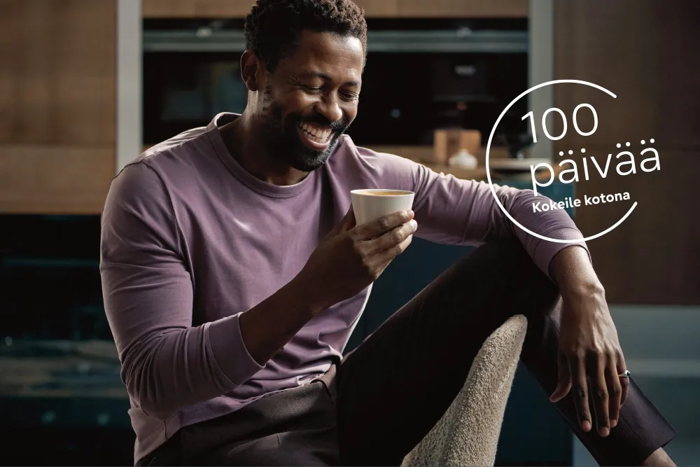 Mies istuu kahvikuppi kädessään leveästi hymyillen. Vieressä teksti "100 päivää Kokeile kotona".